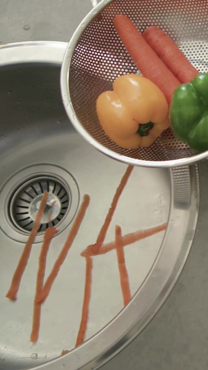 Vertical video: Gripping carrot and Y-peeler, blue-cuffed hands peeling at kitchen sink for cooking