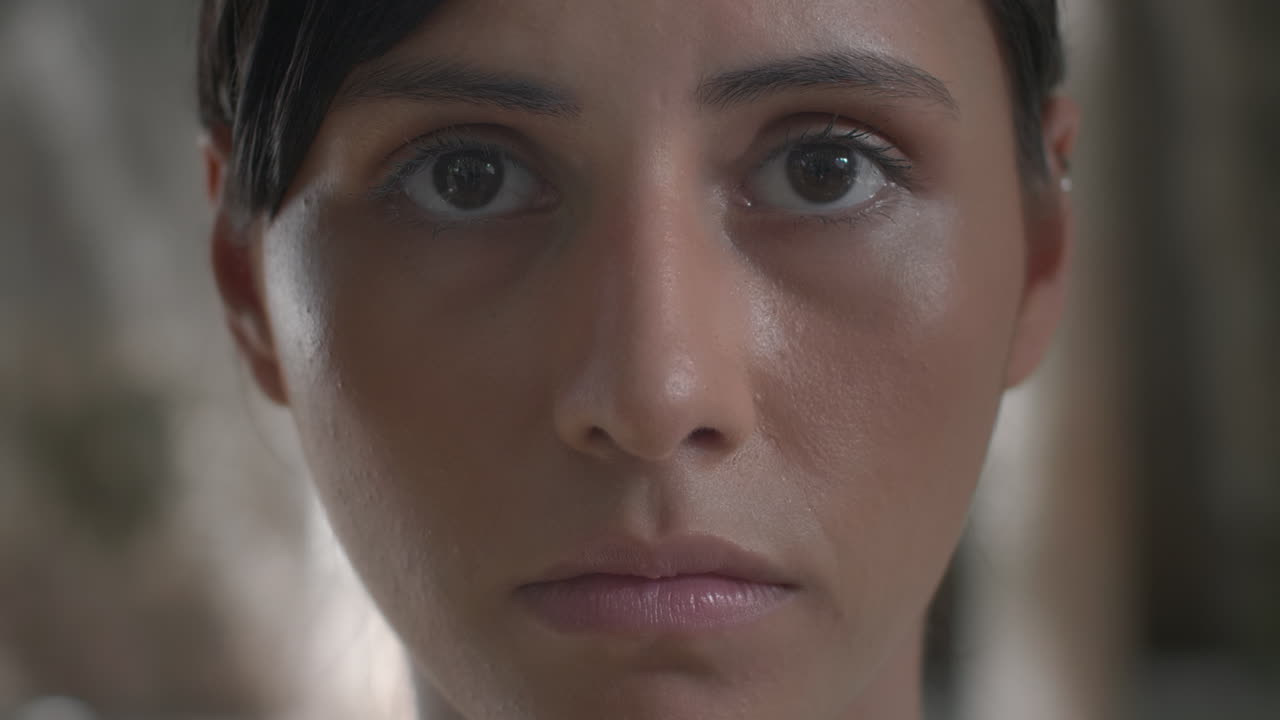 High-quality 4K footage of a serious young woman slowly closing her eyes against a moody, blurred background. Ideal for concentration, trauma, contemplation, or emotional shutdown concepts