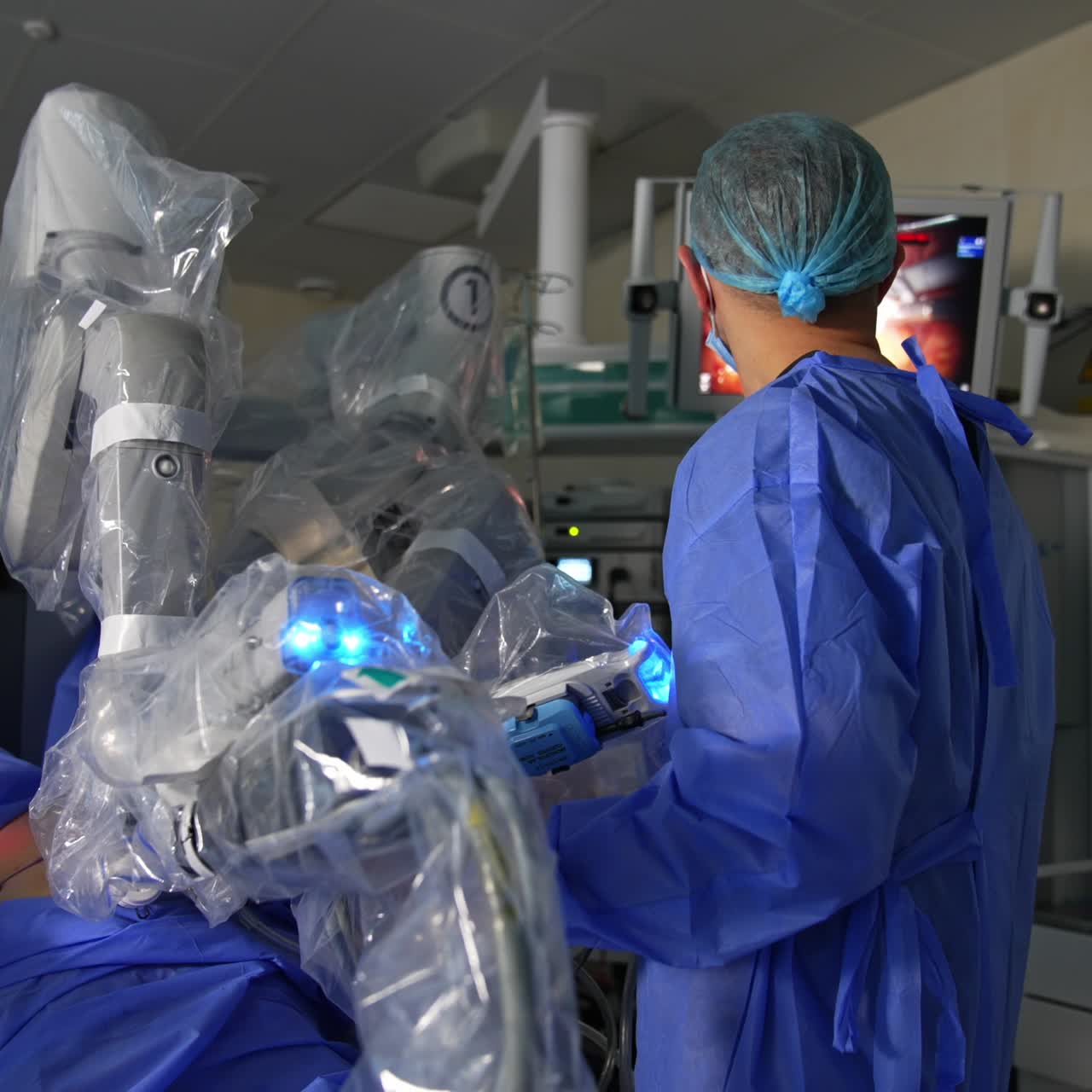 Futuristic robotic equipment working in the modern surgery room. Surgeon stands in operating field looking at the monitor
