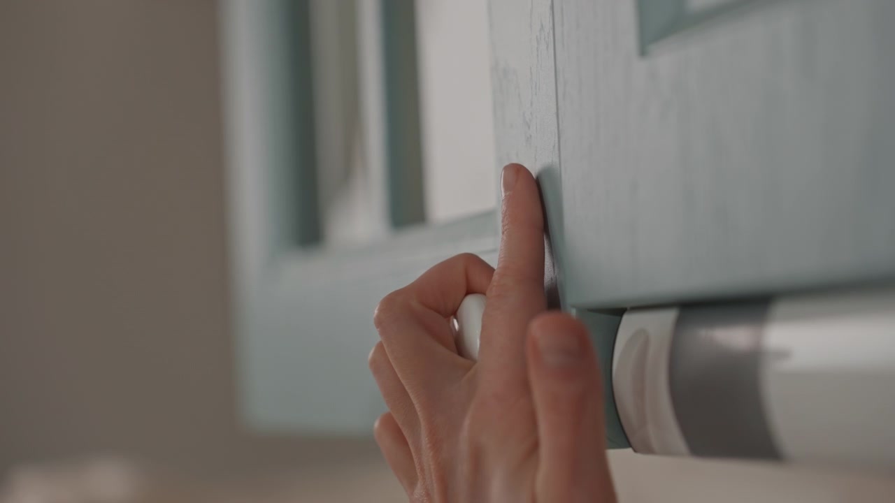 Una mano delicata manipola con cura l'anta di un mobile color verde acqua. Mattina domestica tranquilla con luci rilassanti e suoni lievi. Inizio di giornata sereno caratterizzato da movimenti delicati e un'atmosfera confortevole in casa