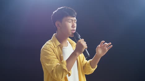 young asian boy holding a microphone and singing on the black background