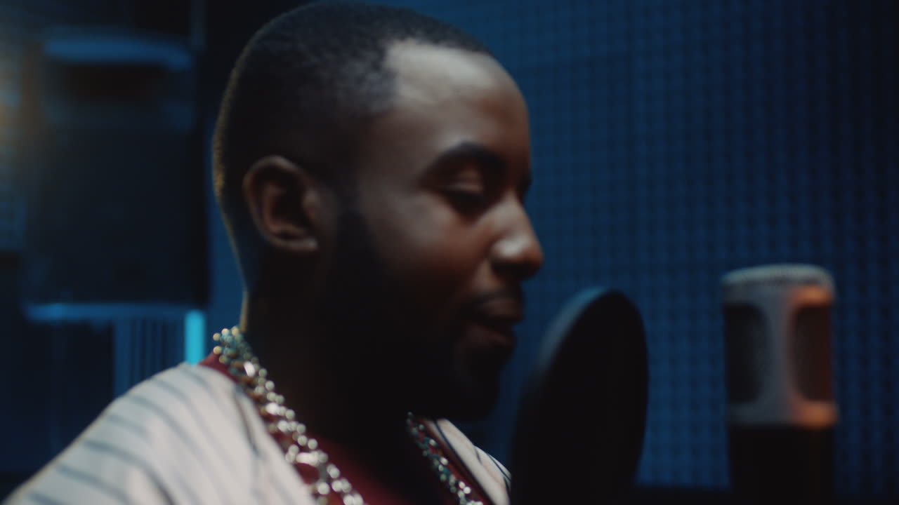 어두운 사운드 스튜디오의 마이크 앞에 서서 카메라를 향해 유쾌하게 웃는 젊은 잘생긴 남성 가수의 초상화