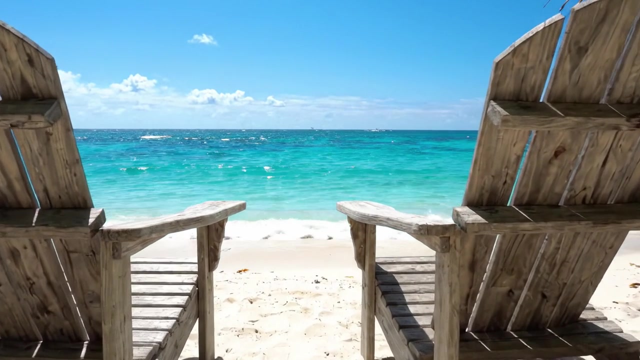 Idyllischer Strandausflug: Eine wunderschöne Szene mit zwei Holzstühlen, die einem ruhigen Ozean unter einem klaren blauen Himmel mit sanften Wellen und goldenem Sand zugewandt sind.