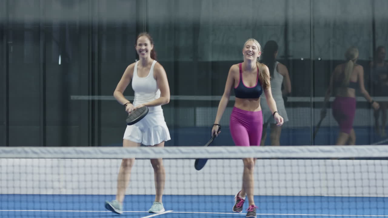 Group of friends enjoying padel tennis match, laughing and holding rackets, on indoor court
