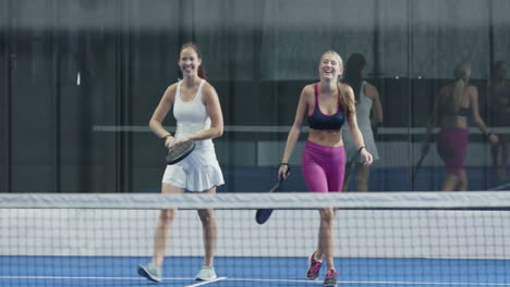 group of friends enjoying padel tennis match, laughing and holding rackets, on indoor court