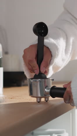 mujer tocando café en un primer plano de portafilter. dama con bata de baño suave llena el recipiente con polvo de espresso en casa. preparación de bebidas energéticas