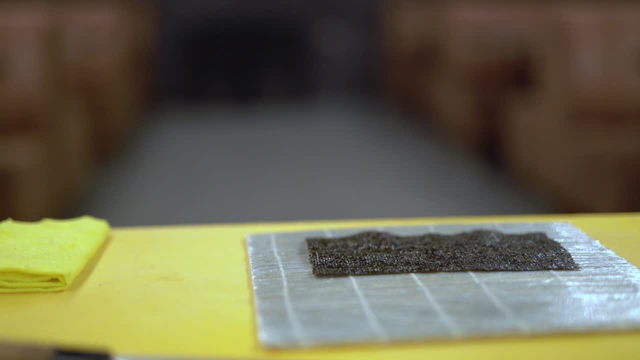 While there is a nori on the rolling mat, a cook prepares a big ball of sushi rice, places it on nori and pushes it to the bottom