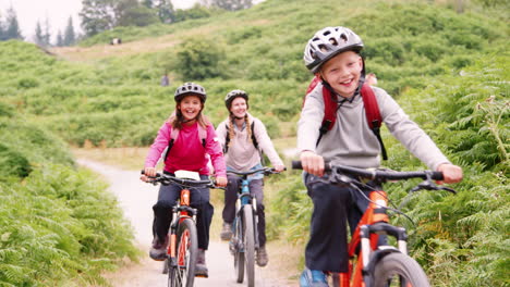 Young-family-having-fun-riding-mountain-bikes-on-a-camping-holiday,-close-up,-front-view,-Lake-District,-UK