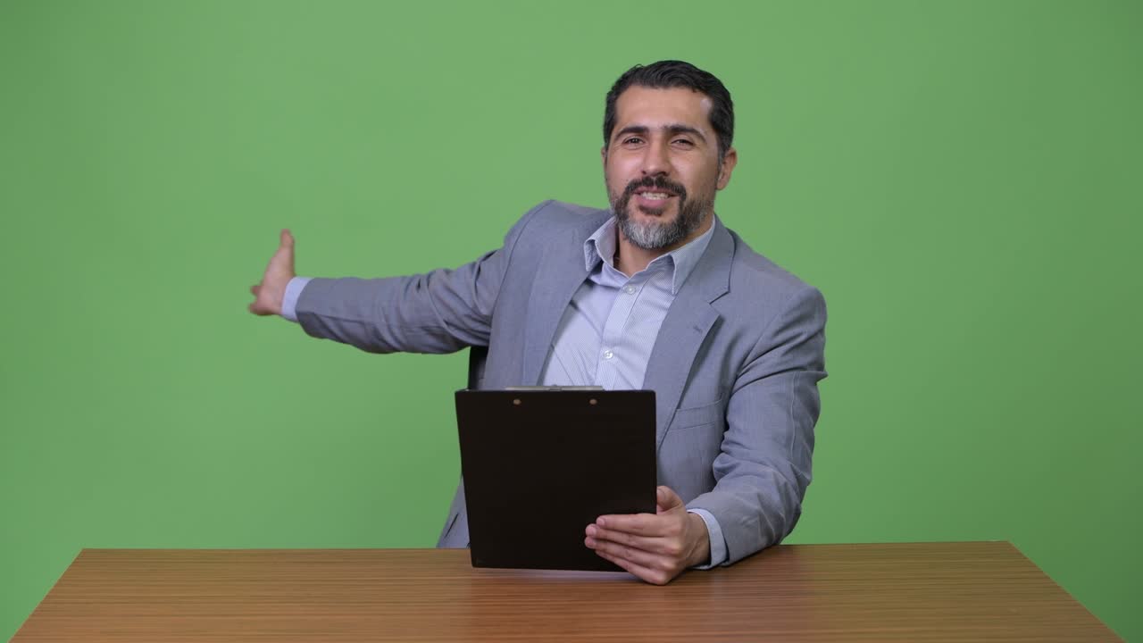Handsome Persian bearded businessman presenting while holding clipboard