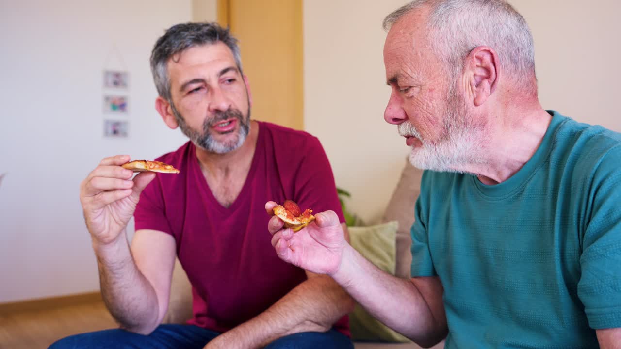 Due uomini che mangiano pizza e parlano su un divano a casa