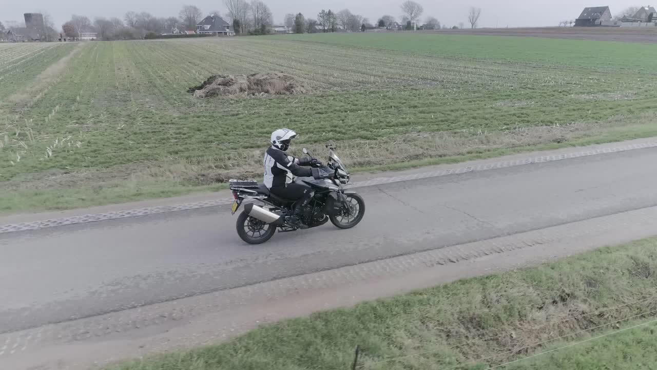 Drone following motorcyclist driving down farm field roads
