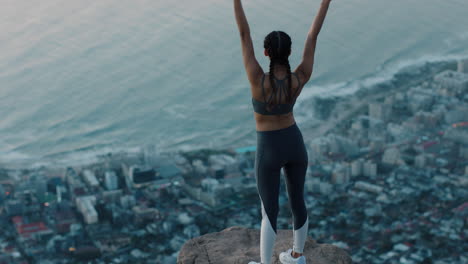 young woman with arms raised on mountain top celebrating achievement girl on edge of cliff looking at beautiful view at sunset enjoying travel adventure