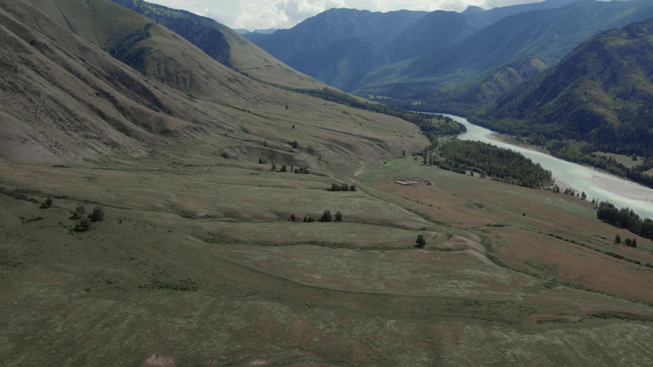 Ampie riprese aeree della Valle di Ak-Kem sui Monti Altai, Russia, con un fiume serpeggiante, pendii verdi e cime distanti sotto una luce estiva nuvolosa