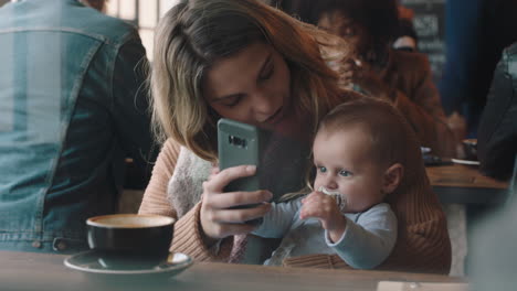 young mother with baby in cafe using smartphone drinking coffee relaxing in busy restaurant enjoying motherhood