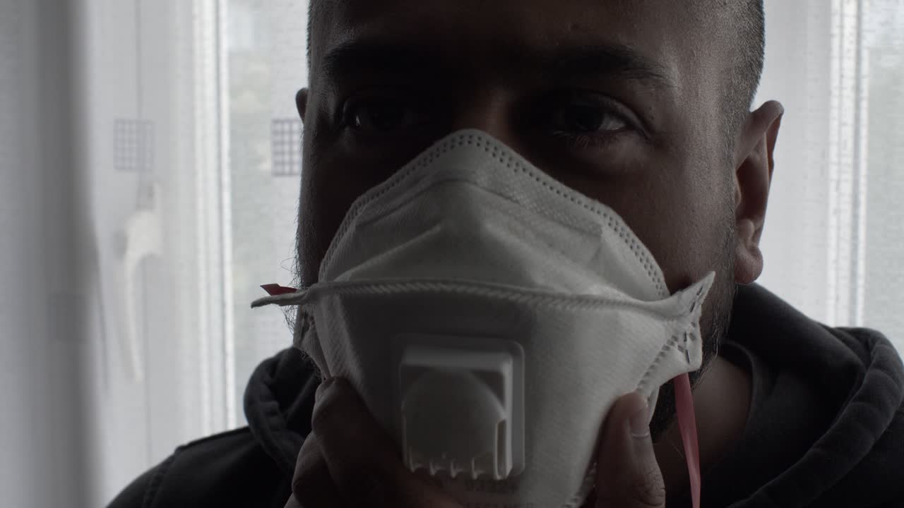 hombre asiático adulto asintiendo con tres máscaras ffp en interiores retroiluminados con la luz del sol de las cortinas