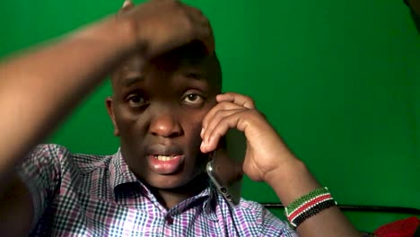dark skinned man calling on phone, working from home office during covid19 pandemic. close up shot with green screen in background.
