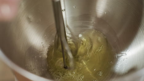close up of electric hand mixer blending egg fluid in stainless steel bowl, capturing spinning motion of beaters and liquid swirl as mixing process creates bubbles and smooth consistency