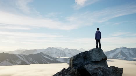 adventurous male hiker standing on dramatic rocky cliff, low clouds and snowy mountain landscape