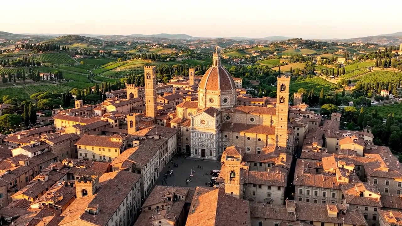 Veduta aerea di un'antica città italiana circondata da rigogliose colline e vigneti al tramonto, catturando lo splendore architettonico e il fascino storico del paesaggio.