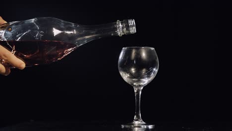 Pouring-pink-champagne-from-bottle-into-glass.-Black-background