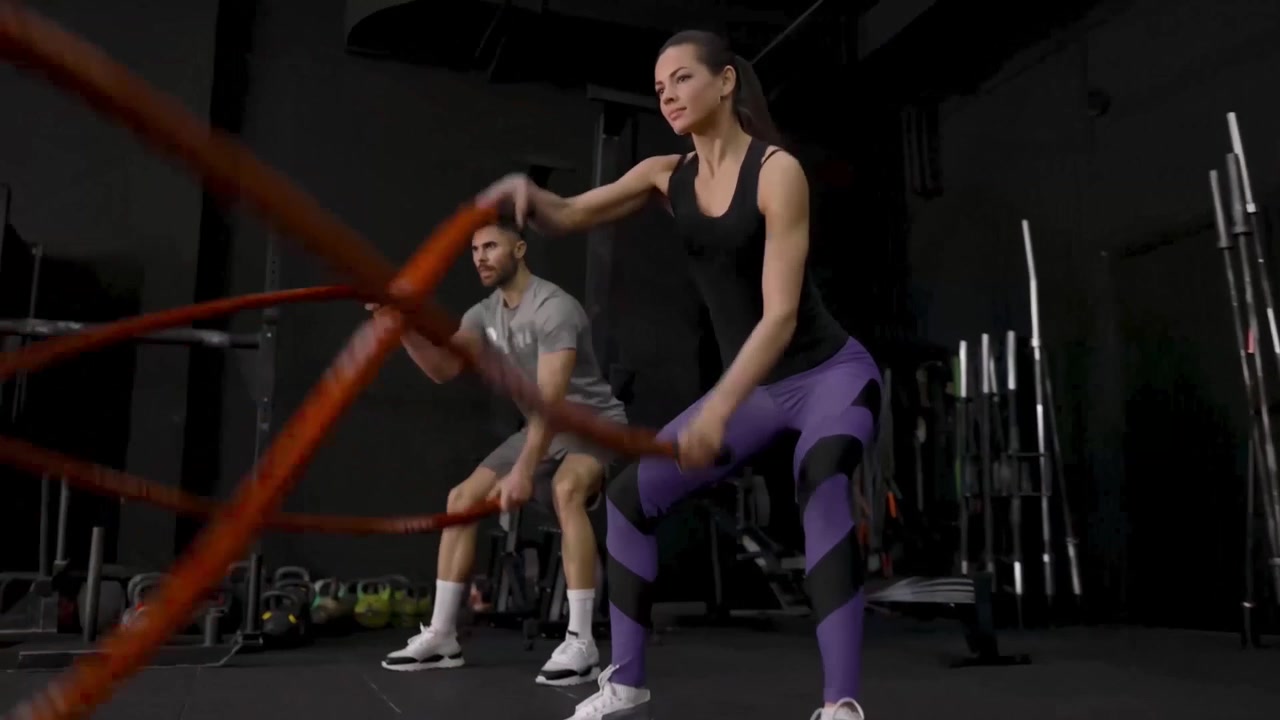 Hombre y mujer ejercitándose con cuerdas de batalla en un gimnasio oscuro
