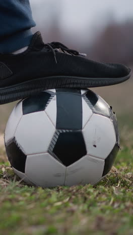 close-up of a person stopping a rotating soccer ball with his left foot on a grassy field, with a blurred background showing a football goalpost