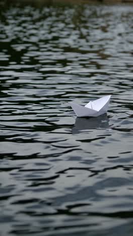 sequence showing a small origami paper boat floating and moving gently on the surface of dark, rippled water, creating a serene and contemplative atmosphere