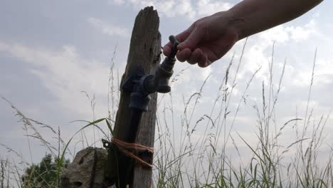 Hand-turning-rickety-faucet-tap-in-farmers-field-medium-shot