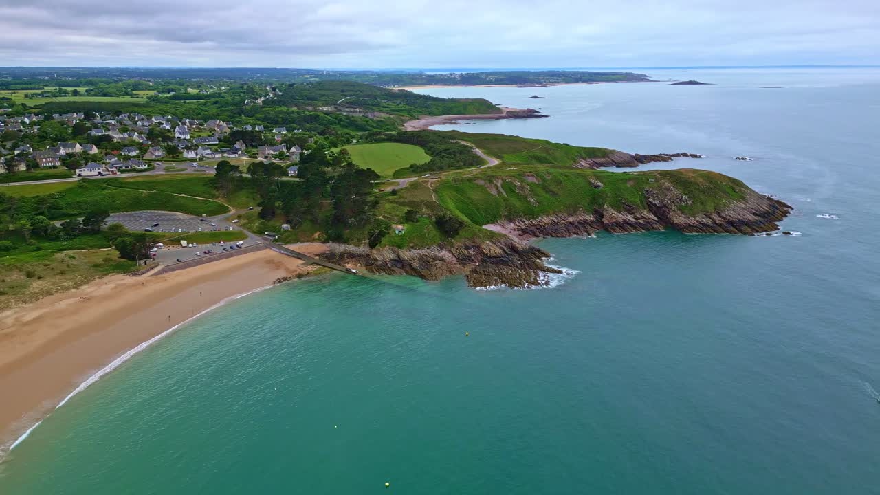 Panoramic drone movement of a lush green coastline with beach and its populated settlement, Pointe aux Chèvres, Brittany, France.