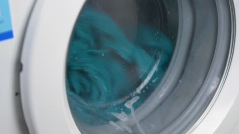 Close-up-slow-motion-shot-of-washing-machine-with-cotton-towels-spinning-cleaning-water-wet-household-chores-laundry-detergent-4K