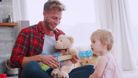 un padre joven tocando el ukelele con su hija pequeña, de cerca