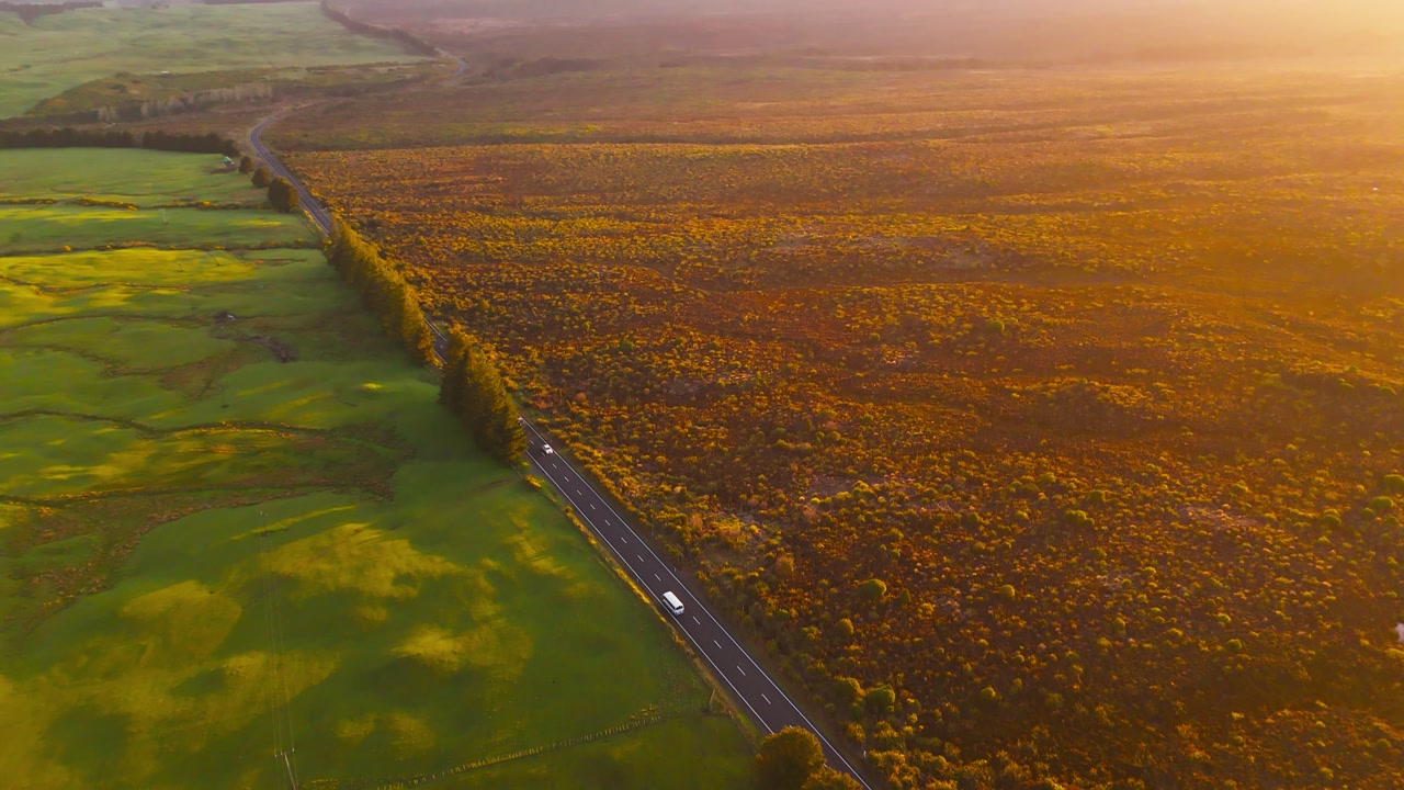 Landscape divides farmland and native scrub at Tongariro National Park, golden hour aerial pan up.