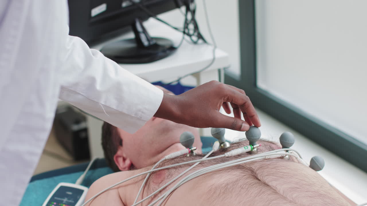 Kardiyoloji test ekipmanı olan bir doktor için hastanın uzuvlarındaki elektrotları takan hastane hemşiresi
