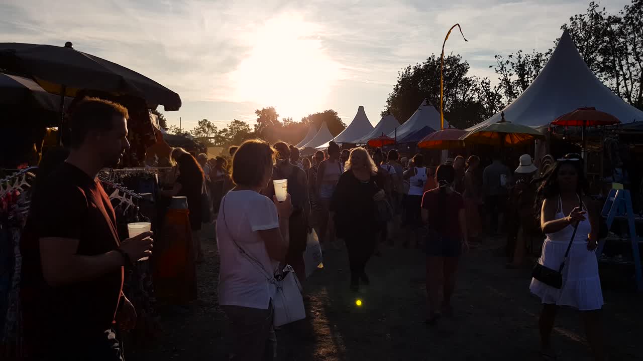 People walking at music festival with tents during sunset