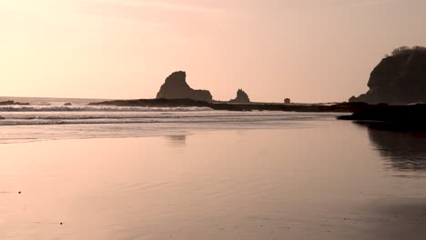 Sunset-at-Playa-Maderas-beach-in-Nicaragua-with-shark-fin-rock-formation,-Handheld-low-shots