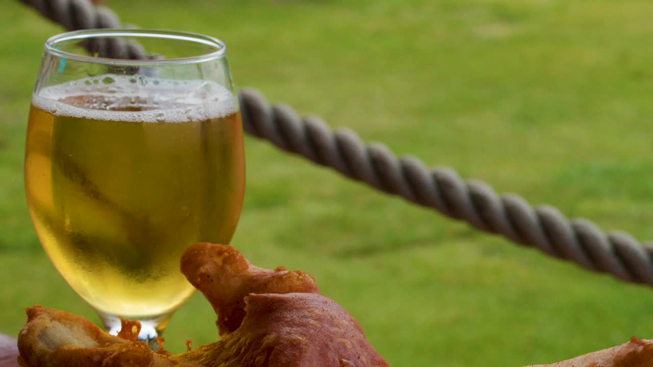 Glass of light beer and roast chicken outdoors on table, natural daylight, shallow focus