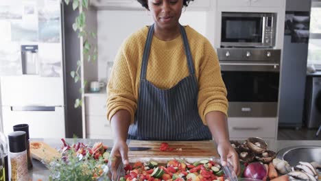happy african american woman in apron preparing meal in kitchen, in slow motion