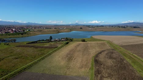 órbita-Aérea-De-Un-Lago-Con-Campos-Circundantes-Y-Un-Claro-Paisaje-De-Montañas-En-El-Estado-De-México,-Almoloya