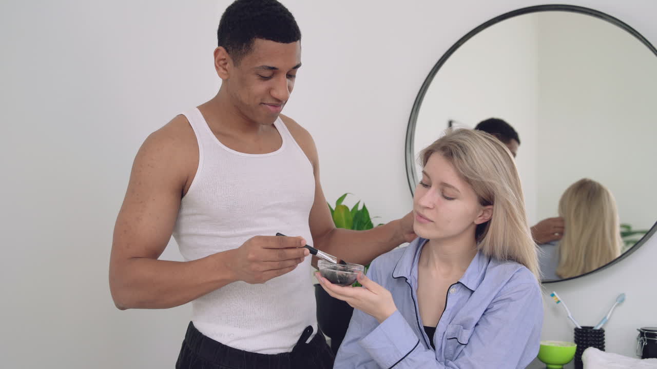 hombre negro guapo aplicando máscara facial a una mujer