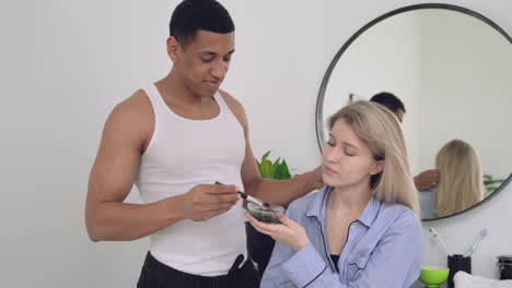 hombre negro guapo aplicando máscara facial a una mujer