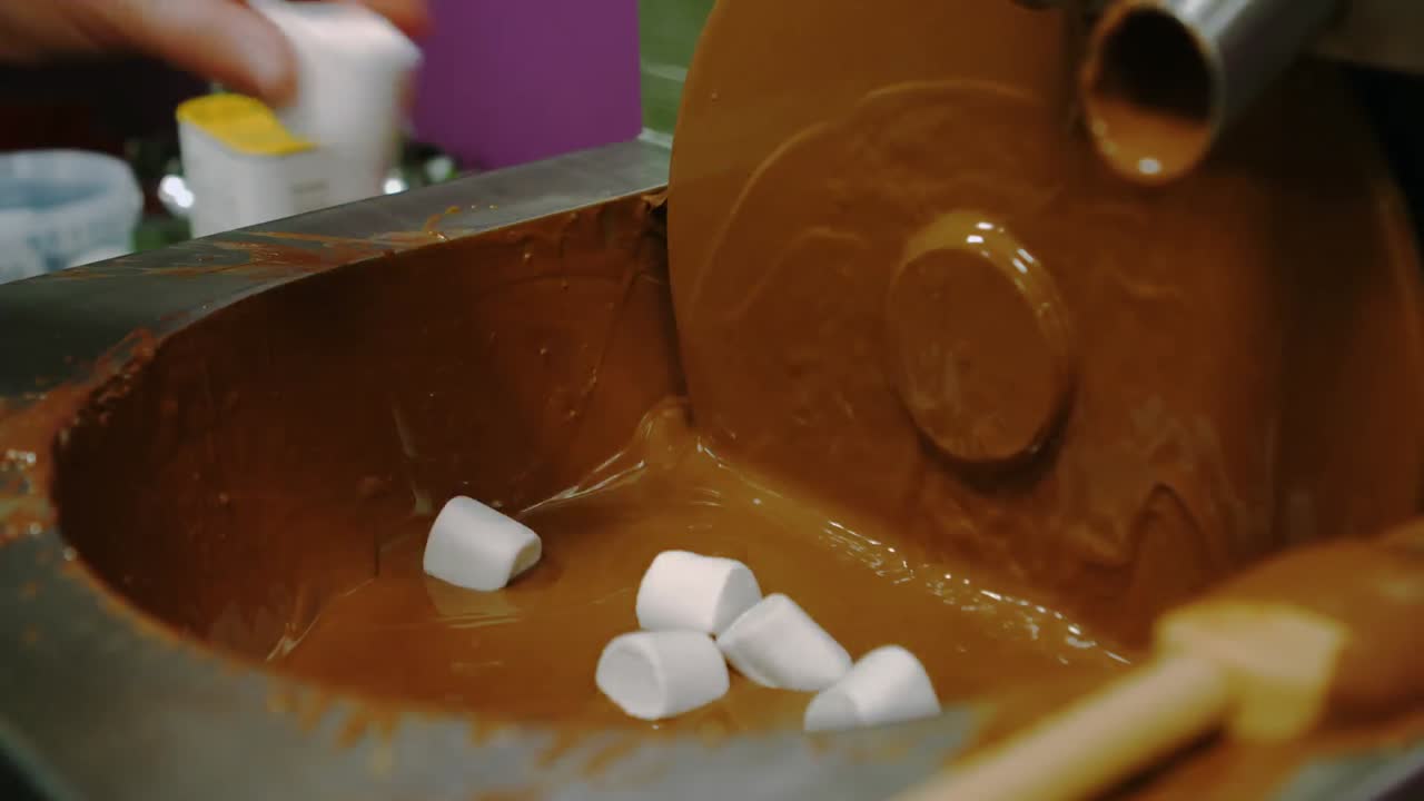 Addetto che intinge un marshmallow con la forchetta nella scioglitrice di cioccolato