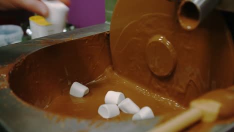 worker dipping marshmallow with fork in chocolate blending machine