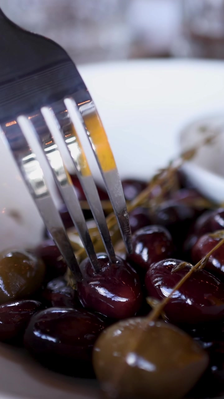 Una forchetta seleziona olive marinate da una ciotola bianca, mettendo in risalto texture e riflessi con un'illuminazione soffusa.