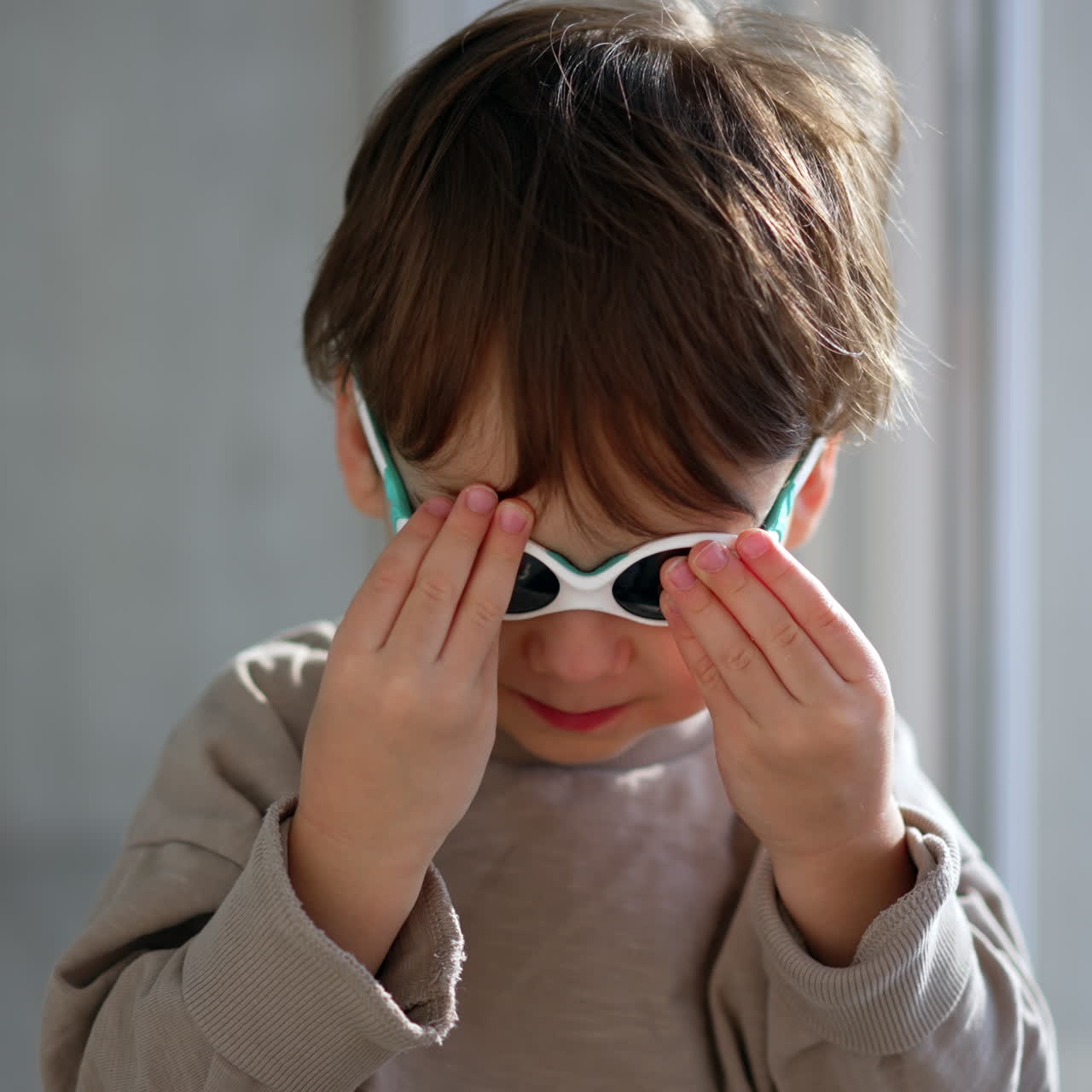 Grazioso bambino con maglione grigio e occhiali da sole. Ritratto ravvicinato del bambino al chiuso.