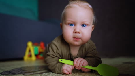 cute blond baby boy lies on the floor chewing a toy. adorable kid approaches the camera but it distances quickly and the kid is surprised.