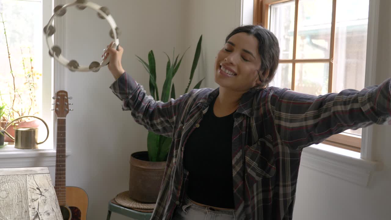 joven músico del caribe confiado chica sacudiendo y bailando al ritmo de la pandereta en casa