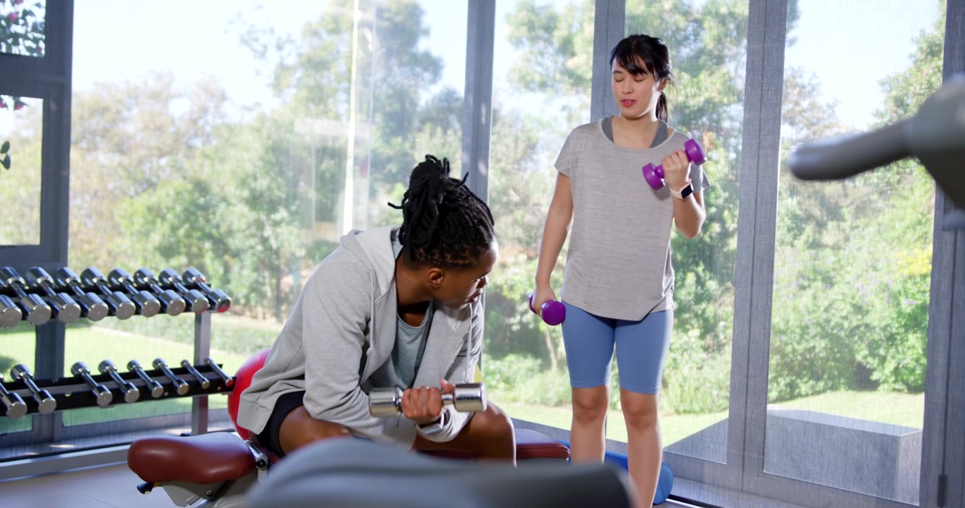 Gym partners starting workout, performing curls with silver and purple dumbbells for strength