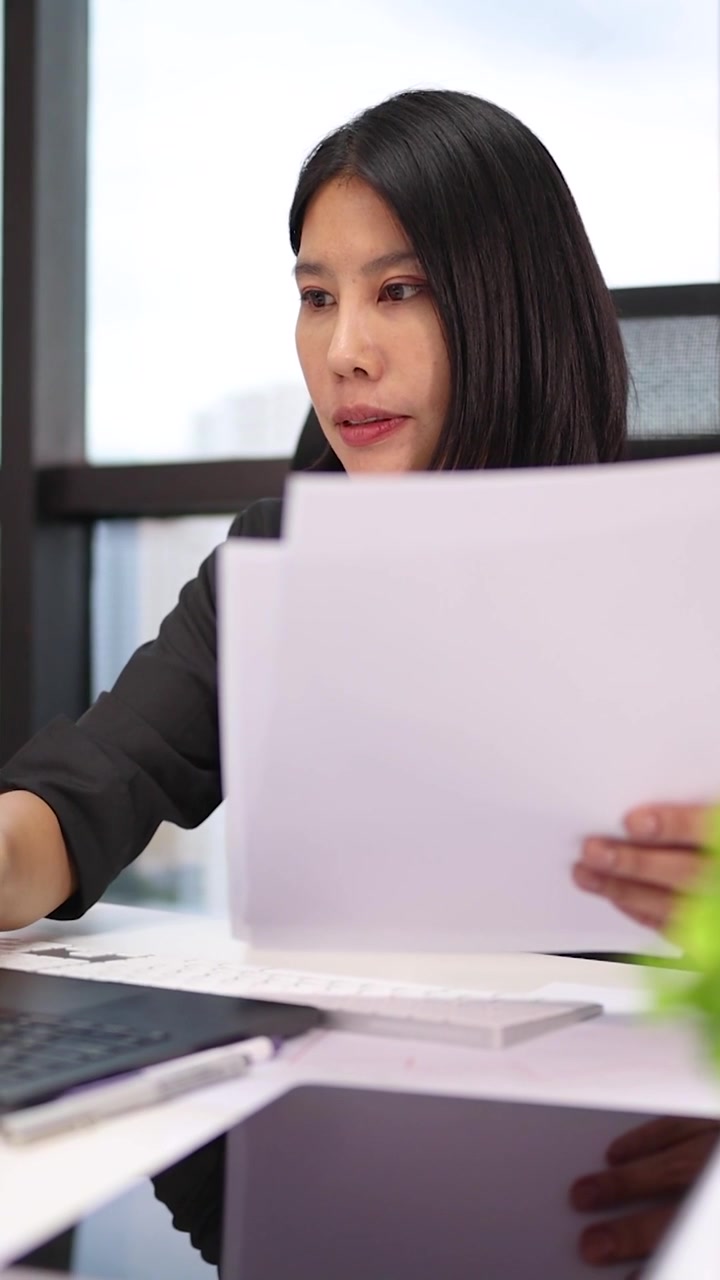Una donna professionista analizza documenti mentre lavora al laptop in un moderno ambiente d'ufficio