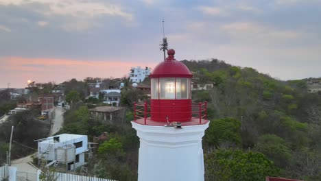 close plane, in orbital trajectory to left, around small lighthouse, with view of sun at sunset