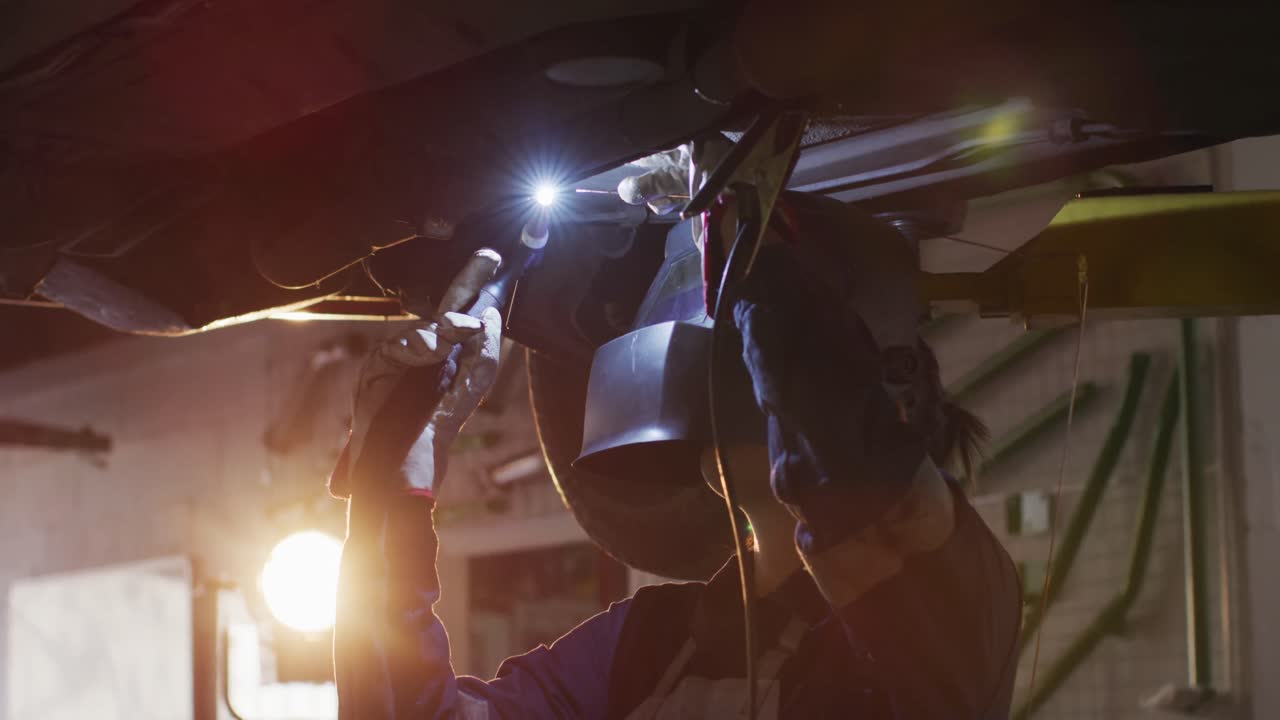Female mechanic wearing welding helmet welding under a car at a car service station